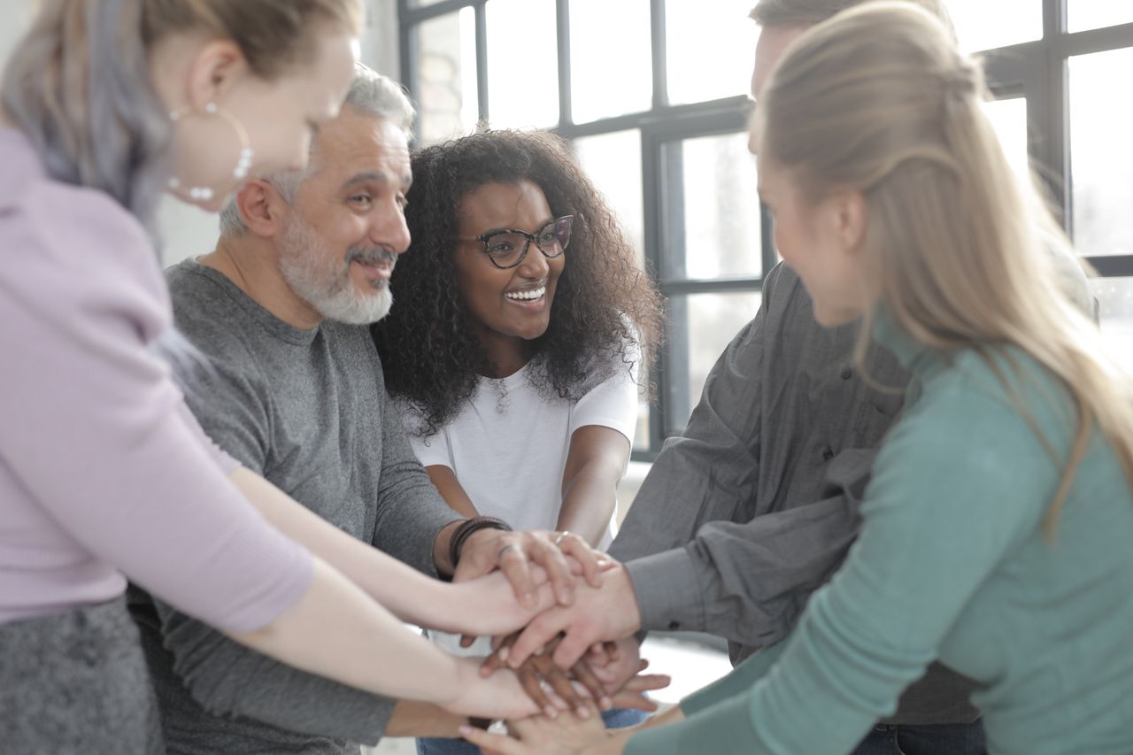 Side view of happy diverse multiracial coworkers uniting hands while standing near fenced window in afternoon and looking at each other